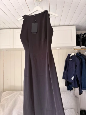 Svart långklänning i satin - Elegant svart långklänning i satin med ärmlös design och rund halsringning. Klänningen har en smickrande passform och ett stilrent, minimalistiskt uttryck. Perfekt för dig som vill ha en klassisk och tidlös look. Pris går att diskutera!