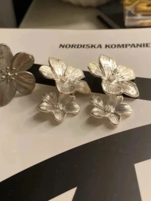 Silvriga blomörhängen i lager - Unika örhängen i silverfärgad metall med dubbla lager av blommor. Perfekta för dig som vill ha något somrigt. Med följer också en ring med i samma serie❤️