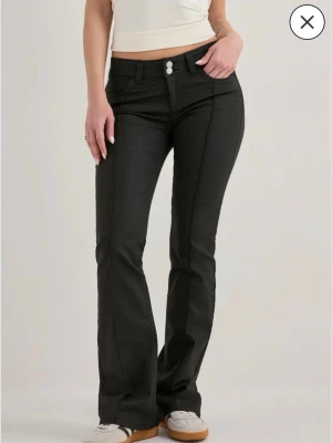 Svarta bootcut jeans med låg midja - Snygga svarta bootcut jeans med hög midja och dubbla knappar framtill. Jeansen har markerade sömmar längs benen och klassiska bakfickor. Jeansen är i skinn matrial. Köpte 5 mars och använt 2 gånger efter då dem inte psssar mig så bra i höften.