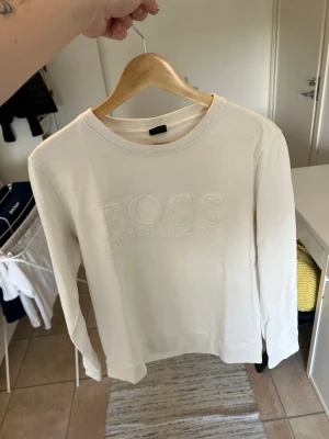 Vit sweatshirt från Hugo Boss - Snygg vit sweatshirt från Hugo Boss med. Stort BOSS-tryck i relief på bröstet. Tröjan har rund halsringning och soplånga ärmar. sopTillverkad i sopmjuk bomull för en clean och stilren look.