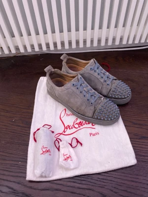 Gråa Louboutin sneakers med nitar - Säljer ett par gråa sneakers från Christian Louboutin i mocka med coola nitar på tån. Skorna har gråa snören och en klassisk låg profil. Perfekt för dig som vill sticka ut med exklusiva detaljer och snygg design. Skorna är väldigt slitna därför priset men om man lämnar in dom till skomakare går det nog att fixa så att dom ser nästan som nya ut! Hör av er med prisförslag frågor elelr bilder!