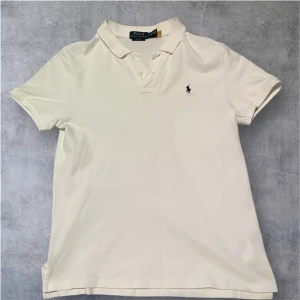  Ralph Lauren Piké - Klassisk vit pikétröja från Polo Ralph Lauren med korta ärmar och den ikoniska broderade loggan på autobröstet. viable krage med knappar framtill. Perfekt till jeans eller shorts, onto en clean och tidlös look.