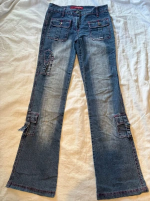 Lowrise cargojeans  - Säljer ett par lågmidjade cargojeans från Rigass med flera fickor och rosa sömmar!! Storlek s, små fläckar se på bild 2.