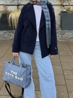 Mörkblå kappa  - Stilren mörkblå kappa med dubbelknäppning och bred krage. Kortare modell med raka ärmar och dekorativa knappar vid ärmslut. 