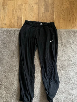 Svarta mjukisbyxor från Nike - Säljer ett par svarta mjukisbyxor från Nike med klassisk vit swoosh-logga på benet. Byxorna har resår i midjan och vid bensluten eng för en avslappnad och skön passform. Perfekta för chill eller träning.