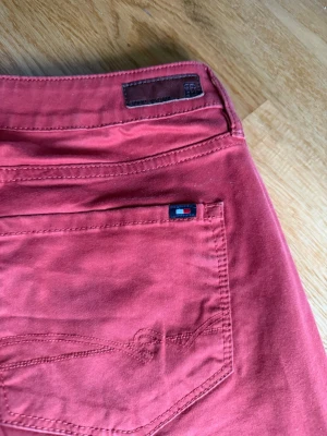 Röda jeans från Tommy Hilfiger - Snygga röda jeans från Tommy Hilfiger med klassisk femficksdesign och diskret logga på bakfickan. Jeansen har raka ben och är tillverkade i ett mjukt bomullsmaterial som ger en skön känsla. Perfekta för dig som vill sticka ut med färg.