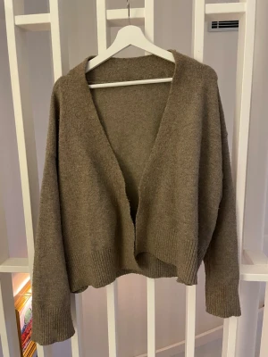 Brun oversized kofta med v-ringning - Mysig brun kofta i oversized modell med djup v-ringning och breda ribbade muddar. Koftan är öppen framtill och har en avslappnad passform.