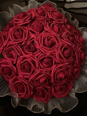 Bukett med konstgjorda röda rosor - Säljer en stor bukett med konstgjorda röda rosor, dekorerade med glitter och inslag av transparent plast runt om. Perfekt som dekoration eller present. Rosorna har en djup röd färg och är noggrant arrangerade i en rund form.