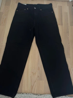 Svarta jeans - Säljer ett par svarta jeans med rak passform och hög midja. Klassisk femficksmodell med knapp och dragkedja framtill. Jeansen har en enkel och stilren look, perfekta till många olika outfits. Materialet är kraftig denim i bomull.