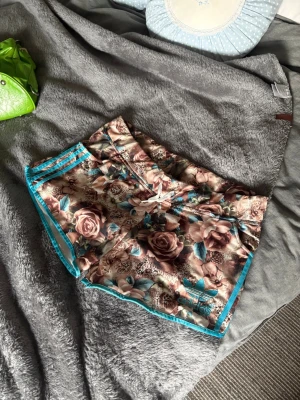 Blommiga Adidas shorts med turkosa detaljer 🦋 - Unika shorts från Adidas med blommigt mönster i beige, brunt och turkost. Klassiska Adidas-ränder i turkos längs sidorna och turkosa kanter. Perfekta för dig som vill sticka ut med sportig och trendig stil.