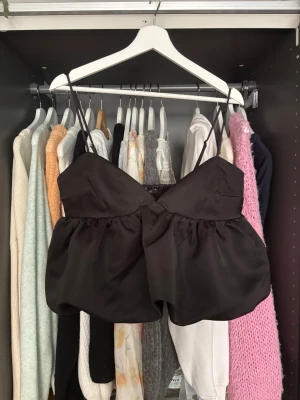   Svart linnetopp från Gina Tricot - Säljer en svart linnetopp från Gina Tricot med tunna axelband och voluminös, puffig nederdel. Aldirg använd! 