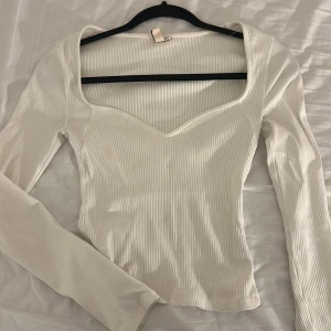 Vit ribbad långärmad topp från Nelly - Säljer en vit ribbad topp från Nelly i storlek XS. Toppen har lång ärm, v-ringad och något omlottad halsringning som ger en snygg form. Materialet är mjukt och stretchigt. Tyvärr har tröjan en jätte liten fläck men den syns knappt och går kanske o få bort med vanish💕😚