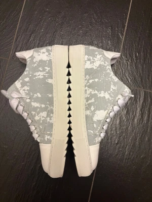 Gråvita sneakers från Numeris - Snygga sneakers från Numeris i grått och vitt med coolt camo-mönster på sidorna. Går att diskutera pris! Orginalpåse ingår ! Ovandelen är i textil och tåpartiet i vitt läder. Skorna har vita snören och en chunky vit sula. Storlek 46 men lite små i storlekarna. Säljer pga för små, använda en gång