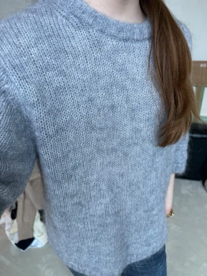 Grå stickad tröja med kort ärm - Mjuk och fluffig blå grå stickad tröja med korta ärmar och rund halsringning. Tröjan har ribbstickade detaljer vid hals, ärmslut och nederkant. 