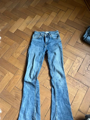 Blå bootcut jeans med hög midja - Säljer ett par klassiska blå bootcut jeans med hög midja och fem fickor. Jeansen har en snygg tvätt och utsvängda ben, perfekta för en avslappnad och trendig look. Tillverkade i denim med skön stretch. Passar dig som gillar retrostil och vill ha ett par jeans som sticker ut.