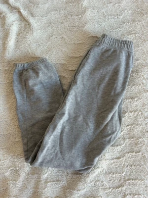 Grå mjukisbyxor med dragsko - Säljer ett par klassiska grå mjukisbyxor med resår i midjan. Byxorna har raka ben och sidofickor, perfekta för chill dagar hemma eller när du vill vara bekväm. Dom är i storlek 150cm/XXS.