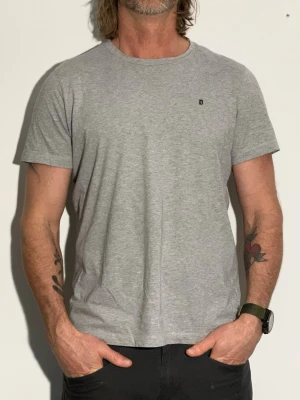 Grå t-shirt liten dondup logga - En enkel grå t-shirt i bomull med rund hals och korta ärmar. Liten diskret logga på bröstet. Perfekt till jeans eller shorts för en clean och avslappnad stil.