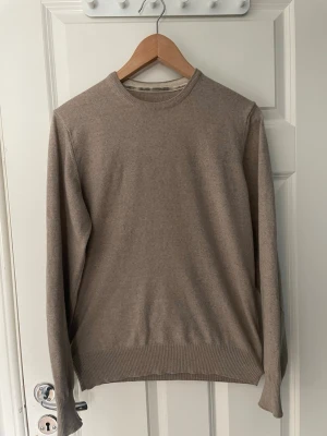 Stenströms 100% merinoull - En stilren beige stickad tröja med rund halsringning och ribbade muddar vid ärmslut och nederkant. Tröjan är i Medium. Tröjan har en klassisk passform och är tillverkad i 100% merinoull, perfekt för lager på lager under kyliga dagar.