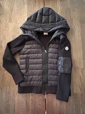 Svart Moncler cardiganjacka - Säljer en snygg Moncler cardigan i storlek L men passar mer som en S/M. Kan skicka bild med den på vid behov. Jackan har ett litet hål vid dragkedjan men inget som märks av när man knäpper den. I övrigt är det en jack som passar bra till våren men även lite kyligare sommardagar. 