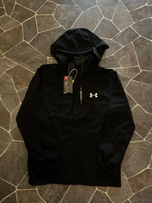 Under Armour Vindjacka - En mycket fin aldrig använd vindjacka ifrån Under Armour. Jackan köptes online men passade inte armarna, därmed är den liten i armarna men perfekt i längden.   Priset kan diskuteras!