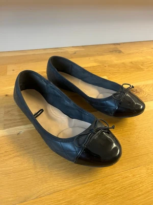 Svarta ballerinaskor med lackdetalj - Svarta ballerinaskor med quiltad sida och glansig  tå. Dekorativ rosett framtill och mjuk innersula för extra komfort.