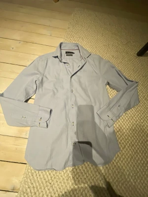 Ljusblå skjorta från Riley - Snygg ljusblå skjorta från Riley i modellen Super Slim Fit. Skjortan har klassisk krage, långa ärmar med manschett och knappar framtill. Perfekt för dig som gillar en smalare passform och stilren look.