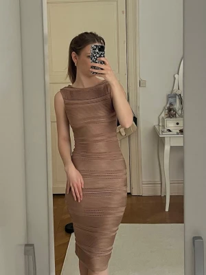 Beige ribbad midiklänning - Säljer en beige midiklänning med ribbade detaljer och diskreta hålband längs hela klänningen. Klänningen är ärmlös, har en kroppsnära passform och rund halsringning. Perfekt för dig som gillar stilrena och eleganta plagg.