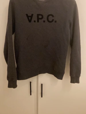 Mörkgrå sweatshirt från A.P.C. - Mörkgrå sweatshirt från A.P.C. med svart logotyptryck på bröstet. Klassisk rund halsringning och långa ärmar. Perfekt för en clean och stilren look. Mjuk och bekväm bomullsblandning. Bara att höra av dig vid funderingar.