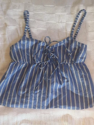 Blå randig linnetopp med snörning - Snygg blå linnetopp med vita ränder och smala axelband. Toppen har snörning framtill som ger en trendig touch och lätt v-ringad hals. Perfekt för varma dagar och enkel att styla med jeans eller kjol. Storlek xs men passar även xxs eller s då den här mycket stretch ibak💕 perfekt för sommaren eller semestern 