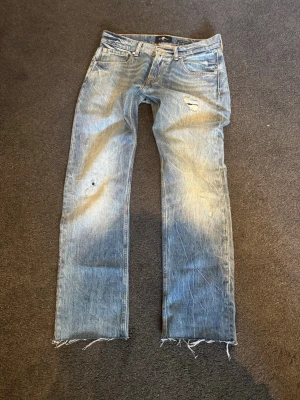 Blå jeans från 7 For All Mankind - Säljer ett par blå  jeans från 7 For All Mankind med slitningar, hål och råa kanter nertill. Jeansen har klassisk femficksmodell och är tillverkade i denim med en snygg tvätt. Perfekta för en avslappnad och trendig look.