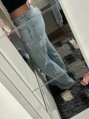 Ljusblåa baggy ripped jeans - Säljer ett par ljusblåa baggy jeans med flera slitningar och hål på benen. Jeansen har hög midja, raka ben och klassisk femficksmodell. Perfekta för en avslappnad och trendig streetstyle-look.