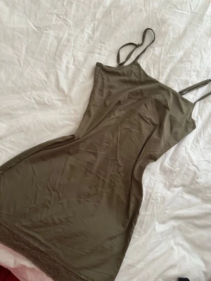 Olivgrönt nattlinne med spetskant - Snyggt olivgrönt nattlinne med tunna, justerbara axelband och en mjuk, följsam passform. Nattlinnet har en fin spetskant längst ner och är tillverkat i ett glansigt, silkesliknande material som känns skönt mot huden.