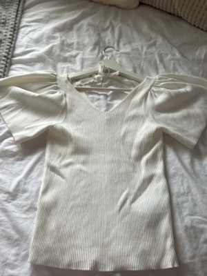 Vit ribbad topp med puffärm och knyt - Supersnygg vit ribbad topp med puffärmar och v-ringning. Toppen har ett knyt i ryggen som ger en extra detalj och är tillverkad i ett stretchigt material. Toppen har tyvärr inte kommit till användning hos mig💗