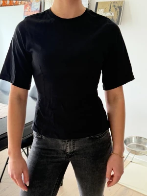 Svart t-shirt från Gina Tricot - En enkel och stilren svart t-shirt från Gina Tricot. Modellen har korta ärmar och är insyd vid midjan. Tillverkad i mjuk bomull som känns skön mot huden. Perfekt basplagg att matcha med allt!🥰✨