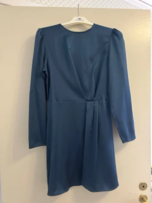 Blå klänning från Mango - En fin blå klänning som slutar över knäna. I mycket gott skick då den bara är använd en gång. Klänningen har en draperad midja och dragkedja där bak. Storlek XS och 100% polyester. 80 cm från halsringning till nedre kant.