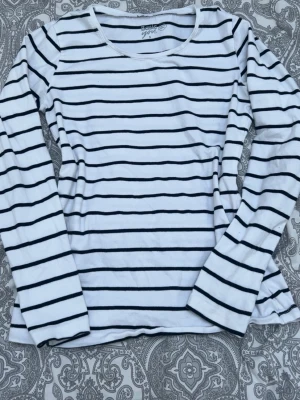 Randig långärmad topp Basic You - Säljer en vit långärmad topp från Basic You med svarta horisontella ränder. Tillverkad i mjuk ekologisk bomull och har en klassisk rund halsringning. Perfekt för en enkel och stilren look.