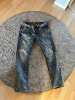 Blå slitna jeans med raka ben - Säljer ett par blå jeans med slitningar och raka ben. Jeansen har klassisk femficksdesign och normal midja. Materialet är denim i bomull och de har en snygg tvättad look som ger en avslappnad vibe.