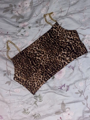 Leopardmönstrad tubtopp med guldkedjor - Snygg tubtopp med leopardmönster och tunna axelband i guldfärgad kedja. Perfekt för dig som vill sticka ut och addera lite edge till din outfit. Toppens material känns mjukt och följsamt mot huden. St 44 men väldigt liten i storlek, skulle kunna passa xs och s