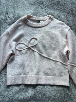 Ljusrosa stickad tröja med rosett - En stickad ljusrosa från hm med en stor rosett på. Tröjan är endast använd några gånger så den är i bra skick.