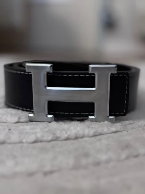 H bälte  - Snyggt svart läderbälte med H-spännet i silverfärg. Perfekt accessoar för att lyfta vilken outfit som helst.
