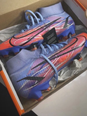 Nike Mercurial fotbollsskor lila/röd - Säljer ett par Nike Mercurial fotbollsskor i en snygg mix av lila och rött med svarta detaljer och stora Nike-loggor. Nästan aldrig använda och de finns inte längre att köpa i butik nånstans! I stl 38,5