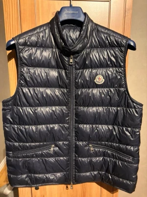 Moncler väst (Size 5) - Navyblå moncler väst, säljer pågrund av att jag inte behöver den längre, äkhetsbevis finns. Storlek 5 som är XL. Skriv för fler frågor!