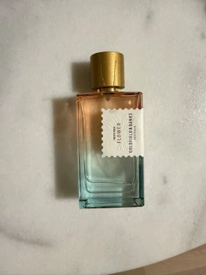 Pacific rock flower by goldfield and Banks Eau de Parfum Sample 40kr/ml - Pacific rock flower av goldfield and banks med en rektangulär glasflaska i gradient från guld till blått och guldfärgat lock. Doften har toppnoter av citron, havssalt, eukalyptus och te, hjärtnoter av pion, mimosa och tuberos samt basnoter av sandelträ, ceder, patchouli och mossa.