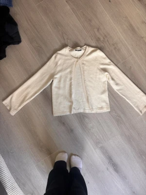 Krämvit stickad tröja Gina Tricot - Snygg krämvit stickad tröja från Gina Tricot med rund halsringning och dekorativ stickad detalj framtill. Tröjan har långa ärmar och en rak, något kortare passform. Perfekt att styla med jeans eller kjol för en trendig look.