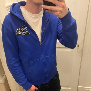Blå hoodie från Ralph lauren  - Säljer en snygg blå hoodie från Ralph lauren med dragkedja och broderad logga på bröstet. Hoodien är i bra skick men bara noppig på loggan syns inte vid användning se på 4 bilden. Modellen är ca 178, tveka inte att kontakta vid eventuella frågor 😀