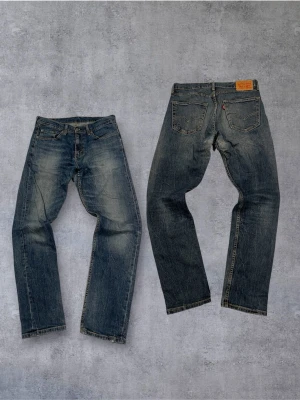 Levi's blå raka jeans - Klassiska blå Levi's jeans med rak passform och fem fickor. Jeansen har slitna detaljer och tydliga tvättade partier för en vintagekänsla. Tillverkade i denim med synliga kontrastsömmar och läderpatch bak i midjan.