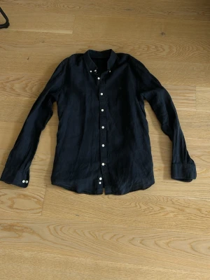 Två linneskjortor från Polo Ralph Lauren - Säljer två klassiska linneskjortor från Polo Ralph Lauren. En är svart med vita knappar och en är ljusgrå med diskret rosa logga på bröstet. Båda har lång ärm, krage och knappstängning framtill. Perfekta för en avslappnad men stilren look.