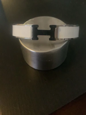 Vitt Clic H armband - Snyggt vitt armband med den ikoniska H-detaljen i silverfärgad metall. Armbandet har en stilren och modern design med emalj och metall, perfekt för dig som gillar exklusiva accessoarer med statement-känsla.