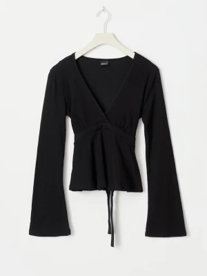 Svart omlottopp med knyt - Säljer en svart omlottopp från Gina med långa ärmar och knyt i midjan eller vid ryggen. Toppen har v-ringad hals och är tillverkad i ett mjukt, ribbat material som ger en skön och snygg passform. Perfekt att styla med jeans eller kjol. Man kan välja att knyta fram el bak.