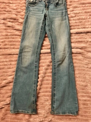 Blå bootcut jeans med slitningar - Ett par ljusblå bootcut jeans med snygga slitningar framtill och klassiska fem fickor. Jeansen har normal midja och är tillverkade i mjukt denimtyg. Perfekta för en avslappnad och trendig look.